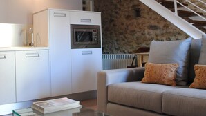 Un soggiorno moderno con una parete in pietra, un divano, un tavolino in vetro e un angolo cottura con forno a microonde.