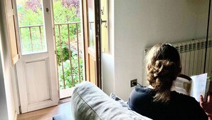Una persona legge un libro in una stanza con un'ampia finestra, un termosifone e un pavimento in legno.