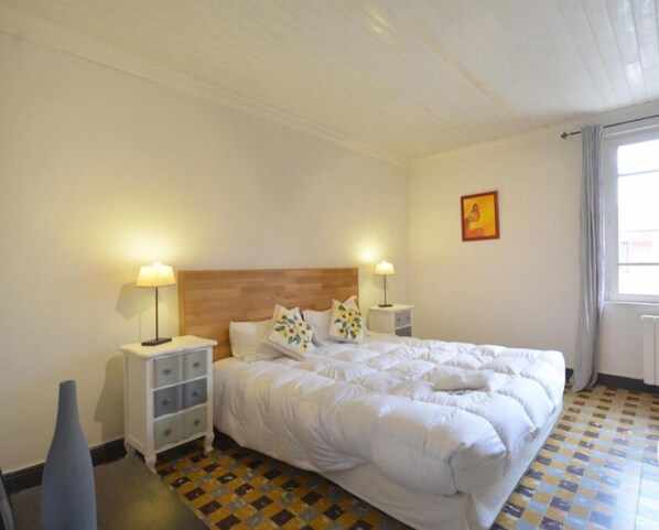 A hotel room with a large bed, two bedside tables with lamps, a small dresser, and a window with curtains.