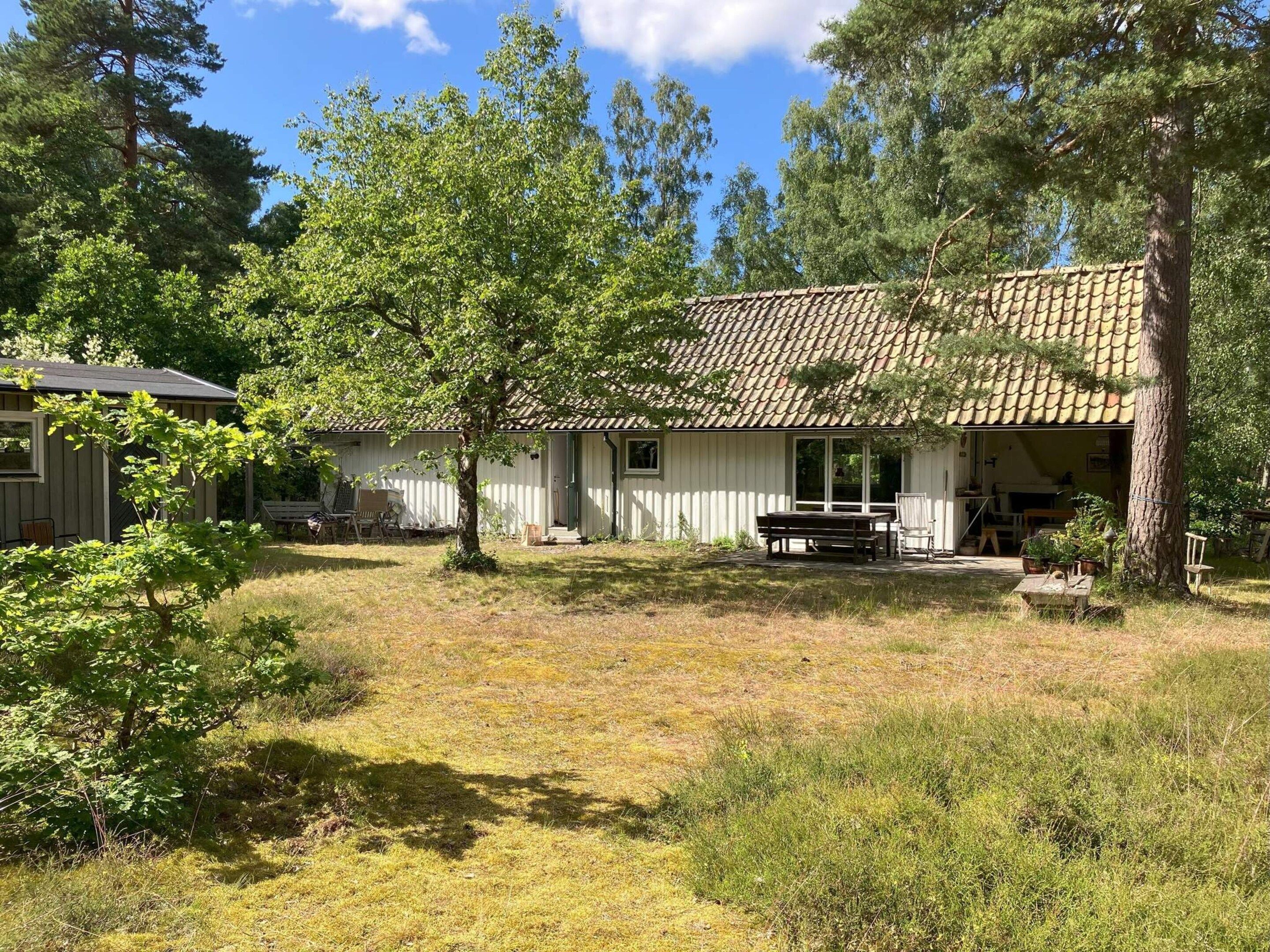 A rustic cabin with a tiled roof, surrounded by trees and a grassy yard.