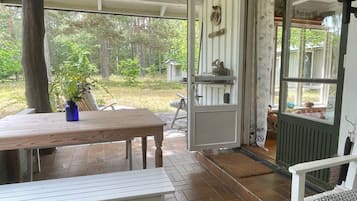Un patio abierto con una mesa y sillas de madera, un jarrón azul con flores, y vistas al follaje circundante.