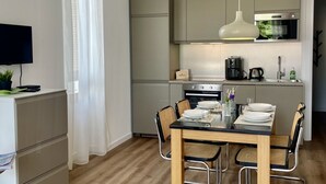A compact kitchen with a dining area, a TV, and a plant.