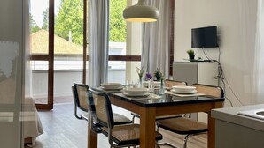 A dining area with a table set for four, a television mounted on the wall, and a view of the outdoors through large windows.
