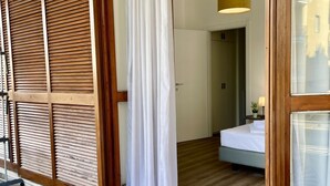 A hotel room with a wooden shingled wall, a bed with a white bedspread, and a small bedside table with a lamp.