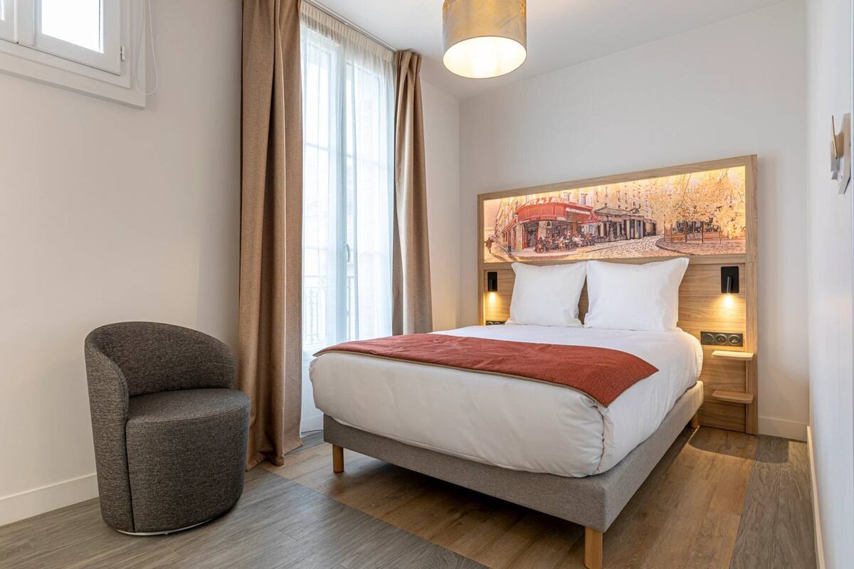 A modern hotel room with a bed, a chair, a large window with curtains, a wall-mounted light, and a cityscape mural.