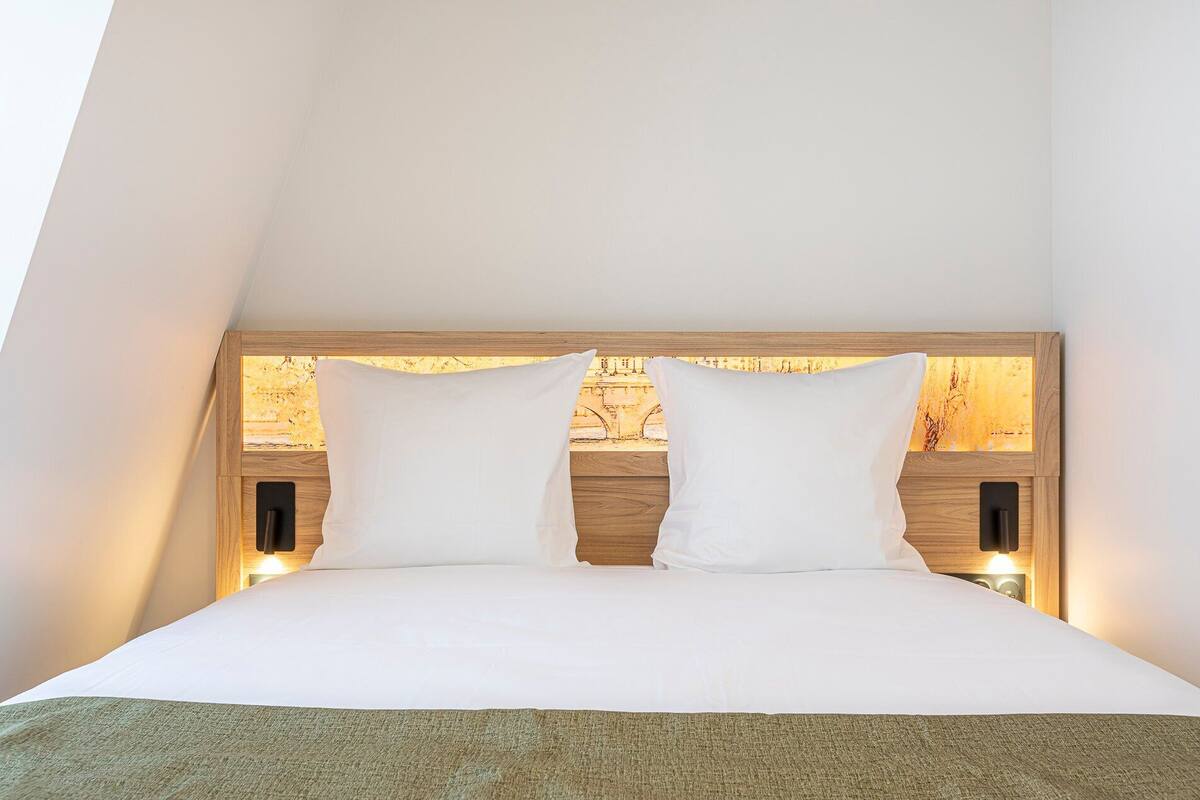 A bed with a wooden headboard, two white pillows, and a green throw blanket.