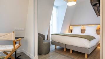 A modern bedroom with a loft-style bed, a small seating area, and a large window providing natural light.