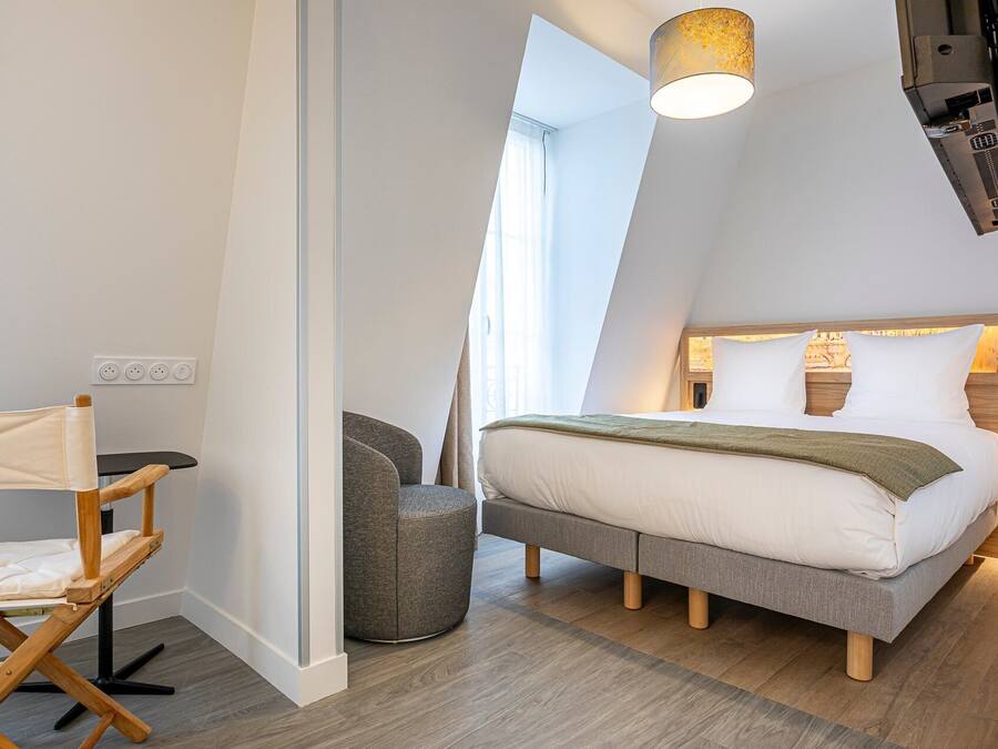 A modern bedroom with a loft-style bed, a small seating area, and a large window providing natural light.