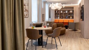 Een moderne eetruimte met een ronde tafel, twee stoelen en een laptop. Er is een boekenkast met diverse items en een zithoek met oranje stoelen.