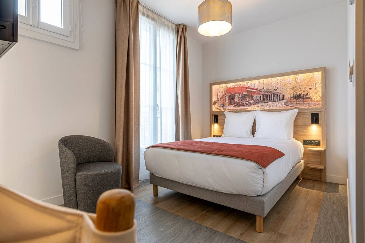 A hotel room with a bed, a chair, a lamp, and a painting on the wall.