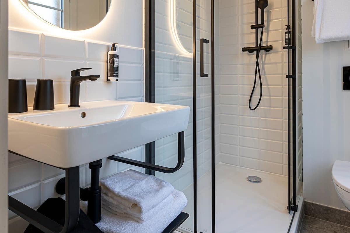 A modern bathroom with a glass-enclosed shower, a white sink with black faucets, and a large mirror.
