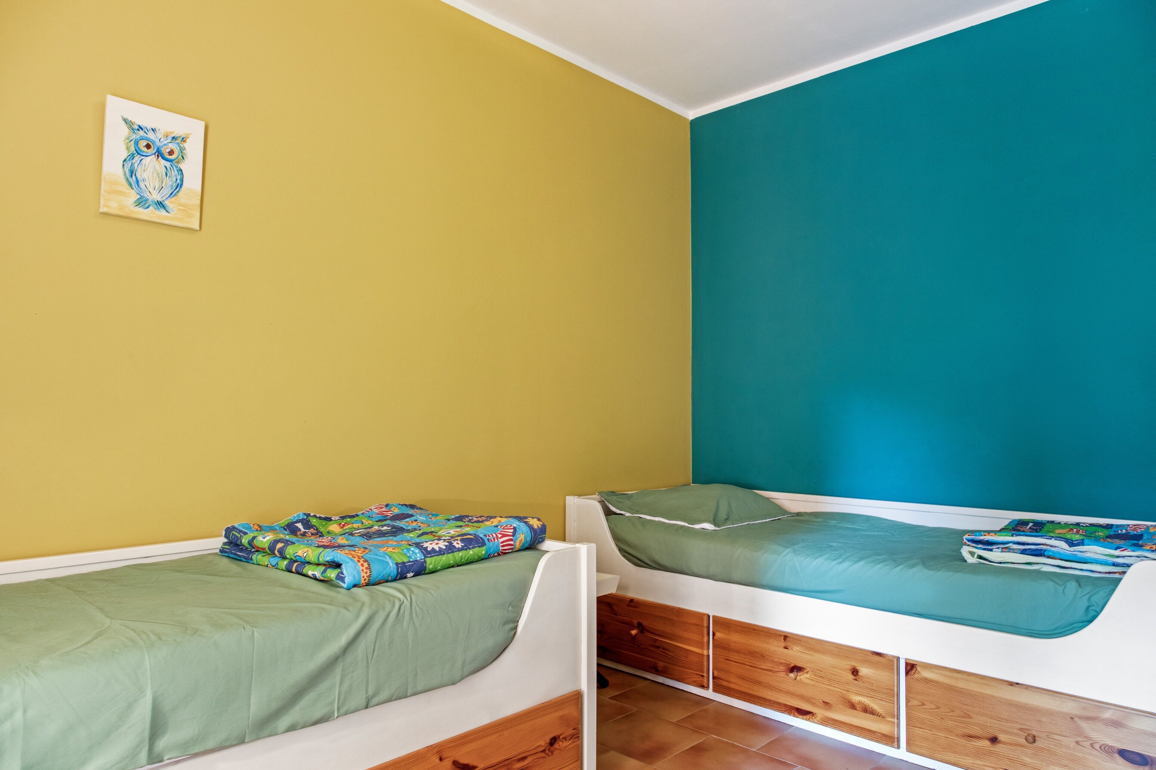 A room with two single beds, a wooden floor, and a painting on the wall.