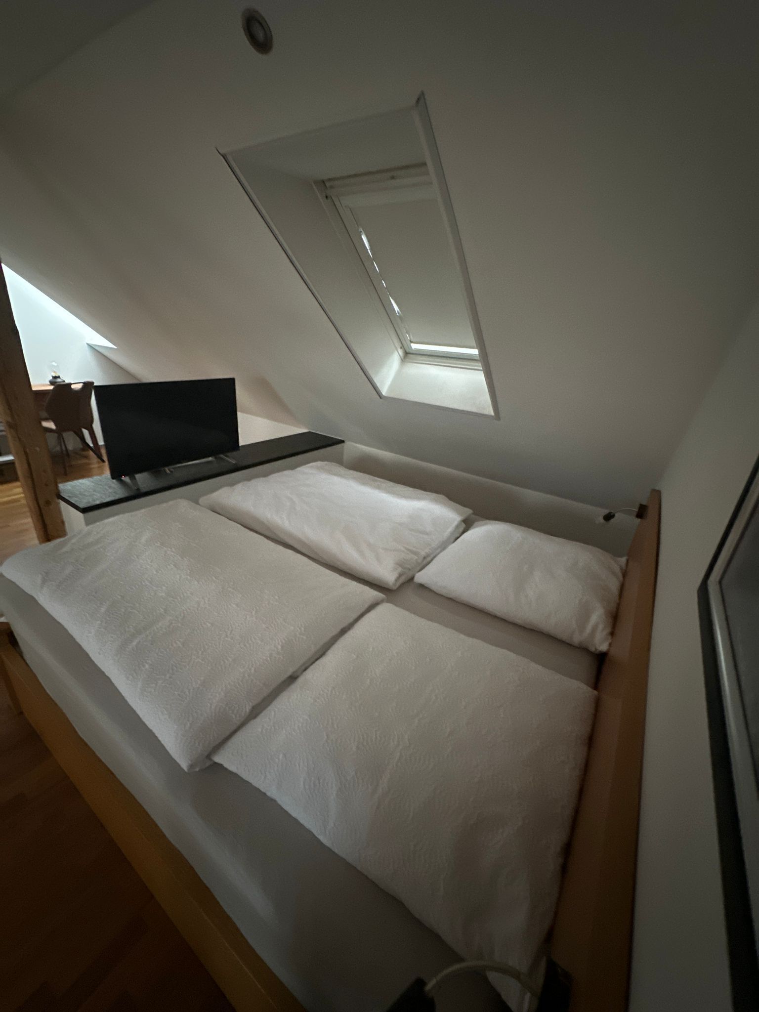 A bedroom with a bed, a desk, and a skylight.
