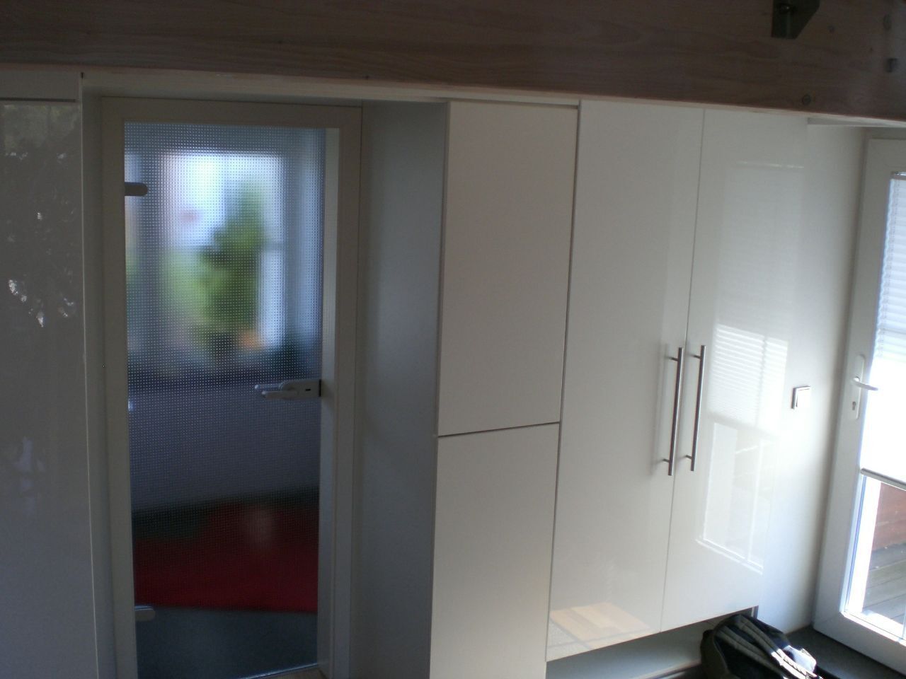 Una habitación con armarios blancos, una puerta con un panel de vidrio esmerilado y una ventana con persianas.