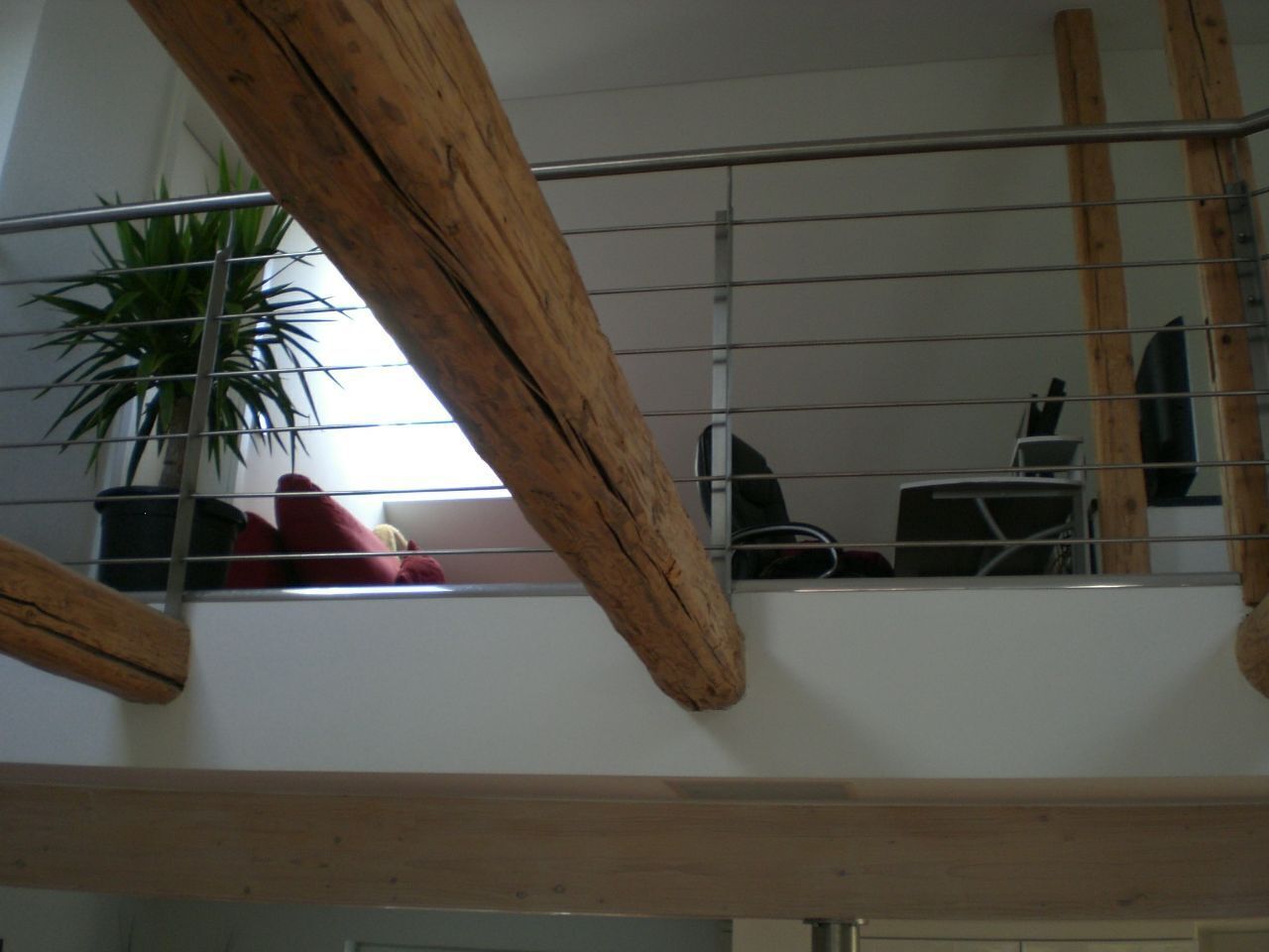 Ein Zimmer mit hoher Decke, Holzbalken, einer Topfpflanze und einem roten Sessel.