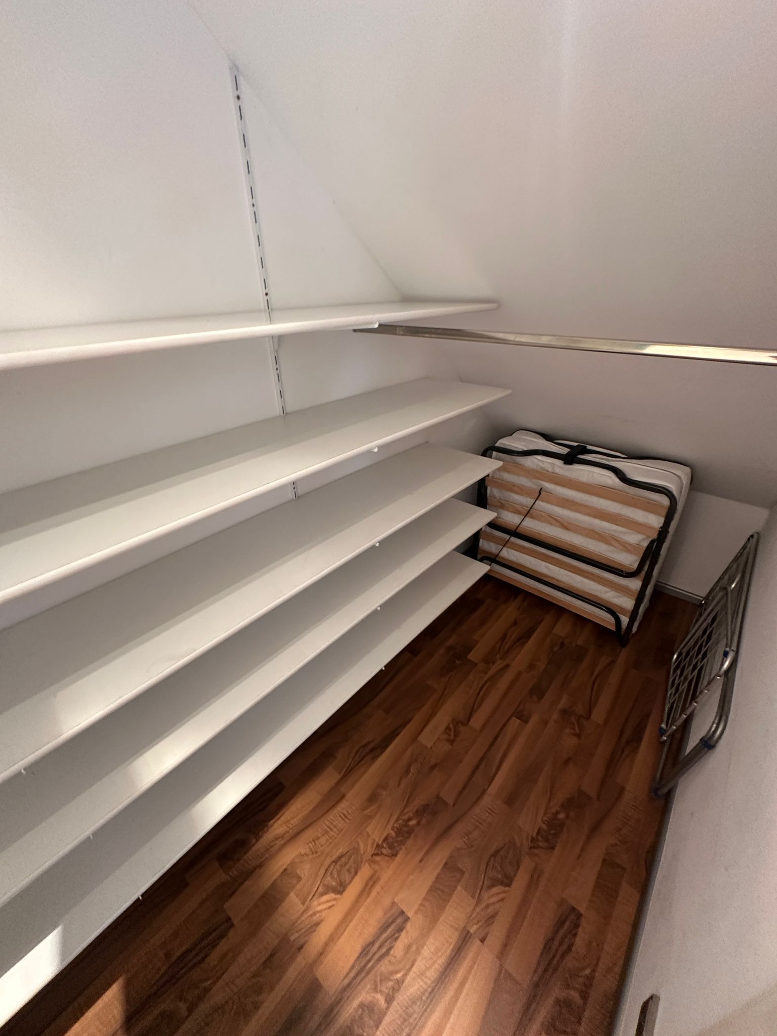 A room with white shelves, a wooden floor, and a metal radiator.