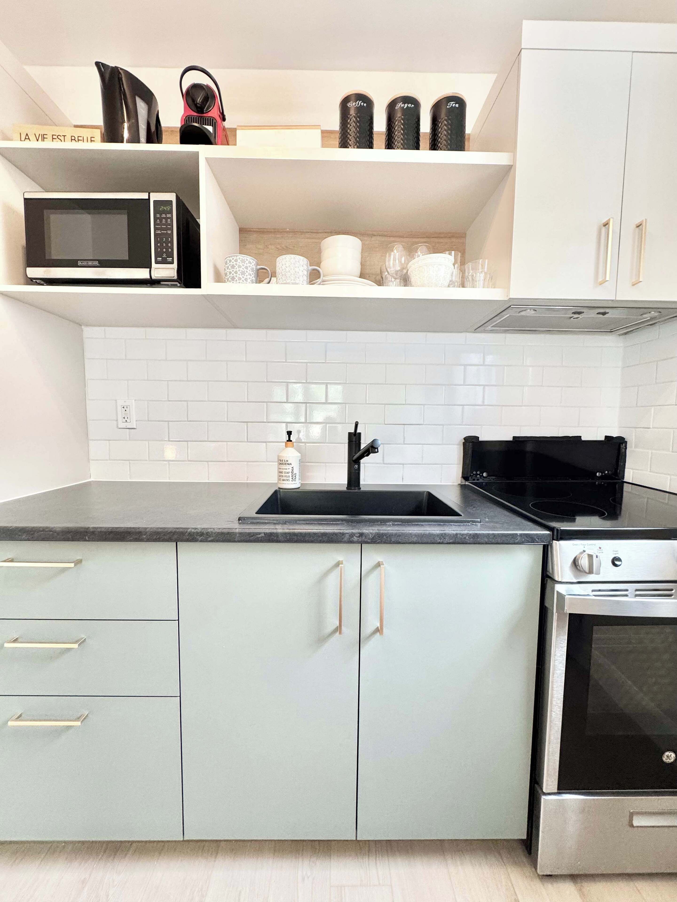 A modern kitchen with white cabinets, a black microwave, a sink, and a stove.
