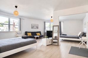 A modern bedroom with two beds, a sofa, a desk, and a mirror.