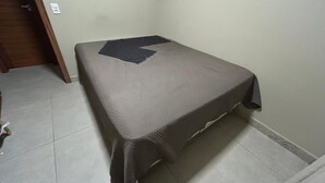 A small, single-bed room with a grey mattress and a dark grey blanket.