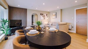 A modern living room with a round dining table set for four, a sofa, a TV, and a large window. - Luxury City Apt with Balcony & Parking (Leeds)