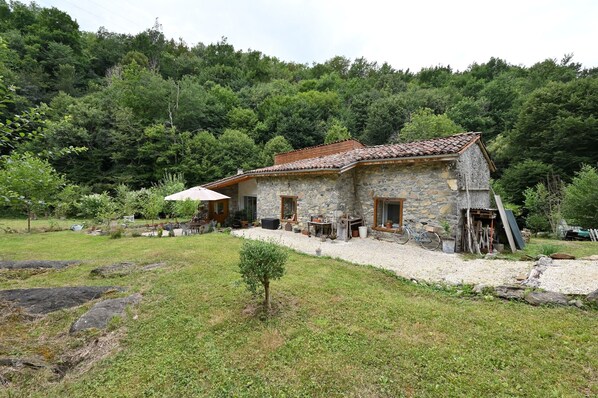 A stone house with a tiled roof, surrounded by a grassy area and trees.
