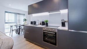 Une cuisine moderne avec des meubles de rangement aux couleurs sombres, un four encastré et un coin repas comprenant une table et des chaises.