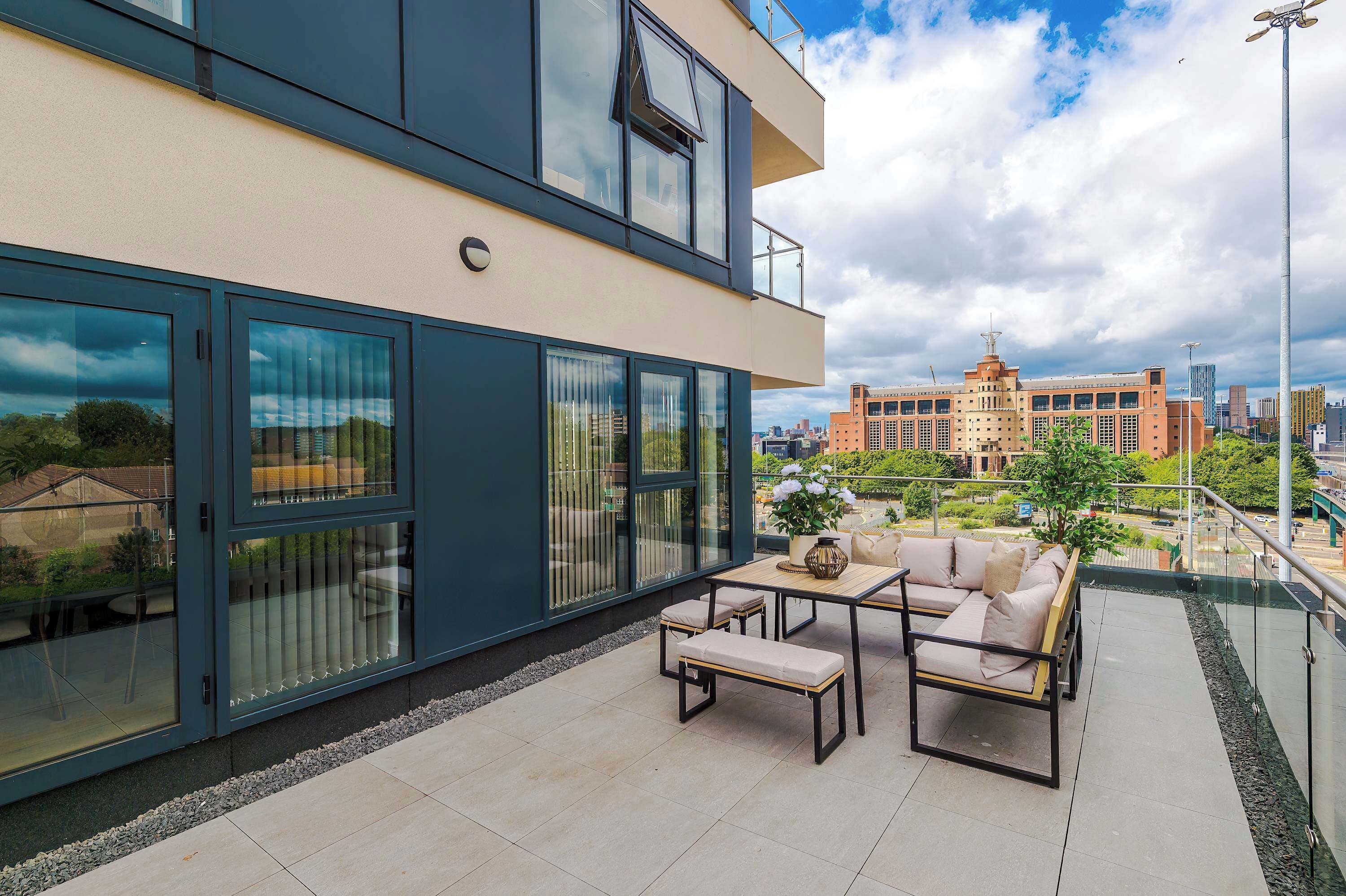 A modern building with large windows, a balcony with outdoor furniture, and a view of a cityscape.