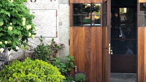 Une porte en bois avec un panneau de verre, un petit balcon doté d’une rambarde en métal et, au premier plan, des plantes en pot.