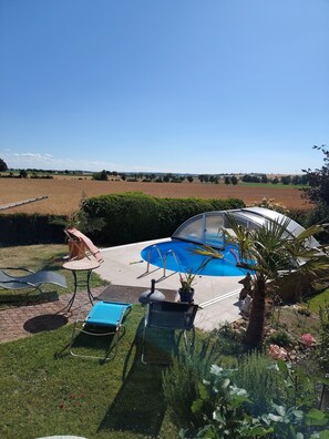 Un patio trasero con piscina, un porche techado y vistas a un paisaje rural.