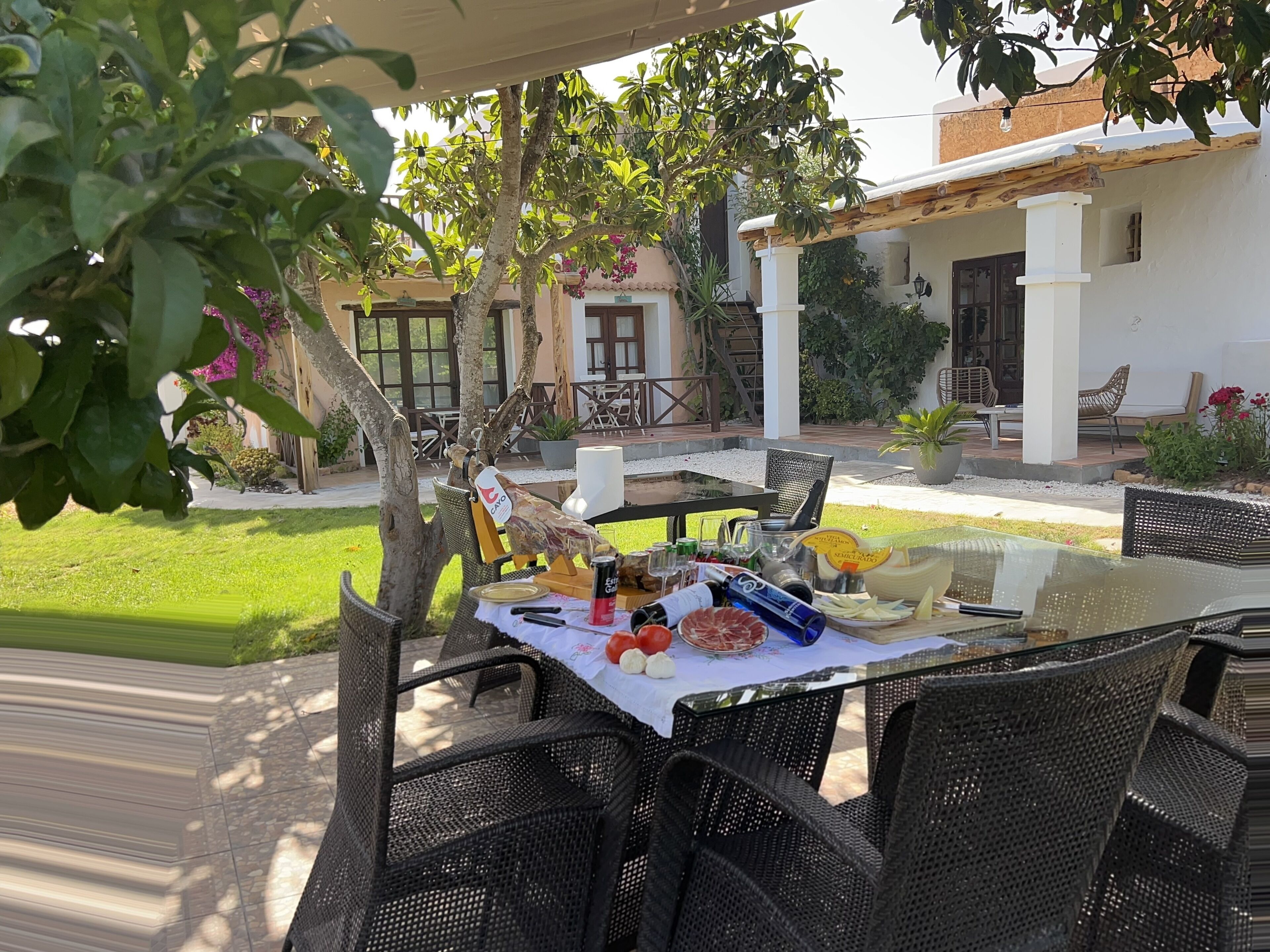 An outdoor dining area with wicker furniture, a glass table, and a variety of food and drink items.