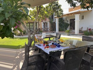 An outdoor dining area with wicker furniture, a glass table, and a variety of food and drink items.
