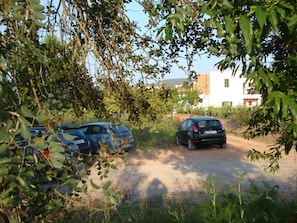 Un espace de stationnement avec deux voitures, entouré de verdure et avec un bâtiment en arrière-plan.