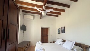 A bedroom with a wooden bed, a ceiling fan, a TV mounted on the wall, and a door. - Finca Can Pepis, surrounded by nature, is ideal for groups of 12 people. (san antonio de portmany)