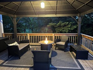 Terraza exterior con zona de estar cubierta, una chimenea y vistas a árboles.