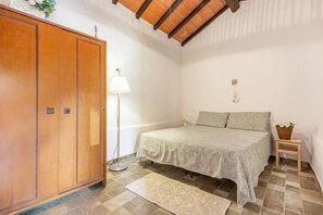 Un dormitorio con cama, armario, lámpara de pie y una mesita con una planta.