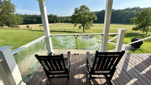 Une terrasse couverte avec deux chaises en bois et une table, donnant sur un champ verdoyant et un étang.