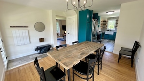 Un coin repas avec une table en bois et des chaises noires, un lustre et une cuisine en arrière-plan.
