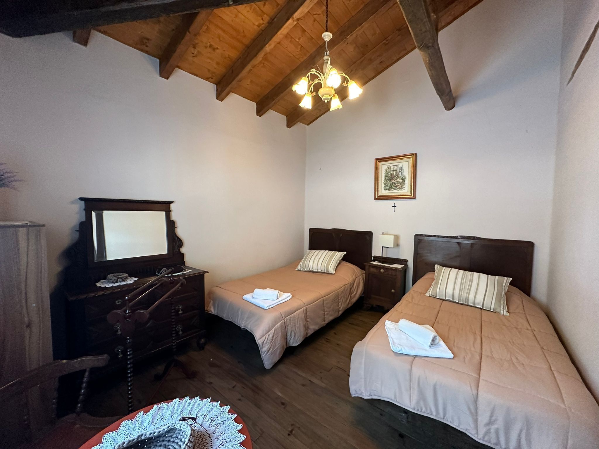 Un dormitorio con dos camas, muebles de madera, una araña y un cuadro en la pared.