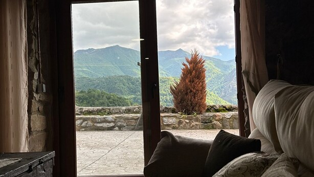 Una habitación con una cama, una pared de piedra y vistas a las montañas a través de una puerta abierta.