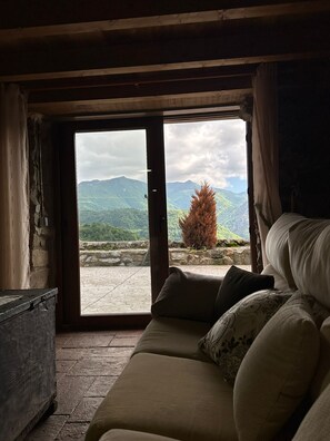 A room with a bed, a stone wall, and a view of mountains through an open door.