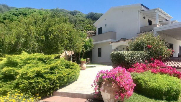 A modern house with a garden path leading to the entrance, surrounded by lush greenery and flowering plants. - Villa Surrounded by Nature Bbq Privacy Sea Relax (Castelsardo)