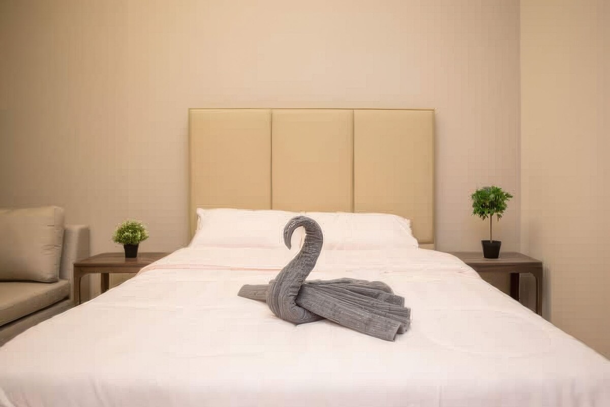 Una cama bien hecha con un almohadón con forma de cisne y dos plantas en macetas a cada lado.