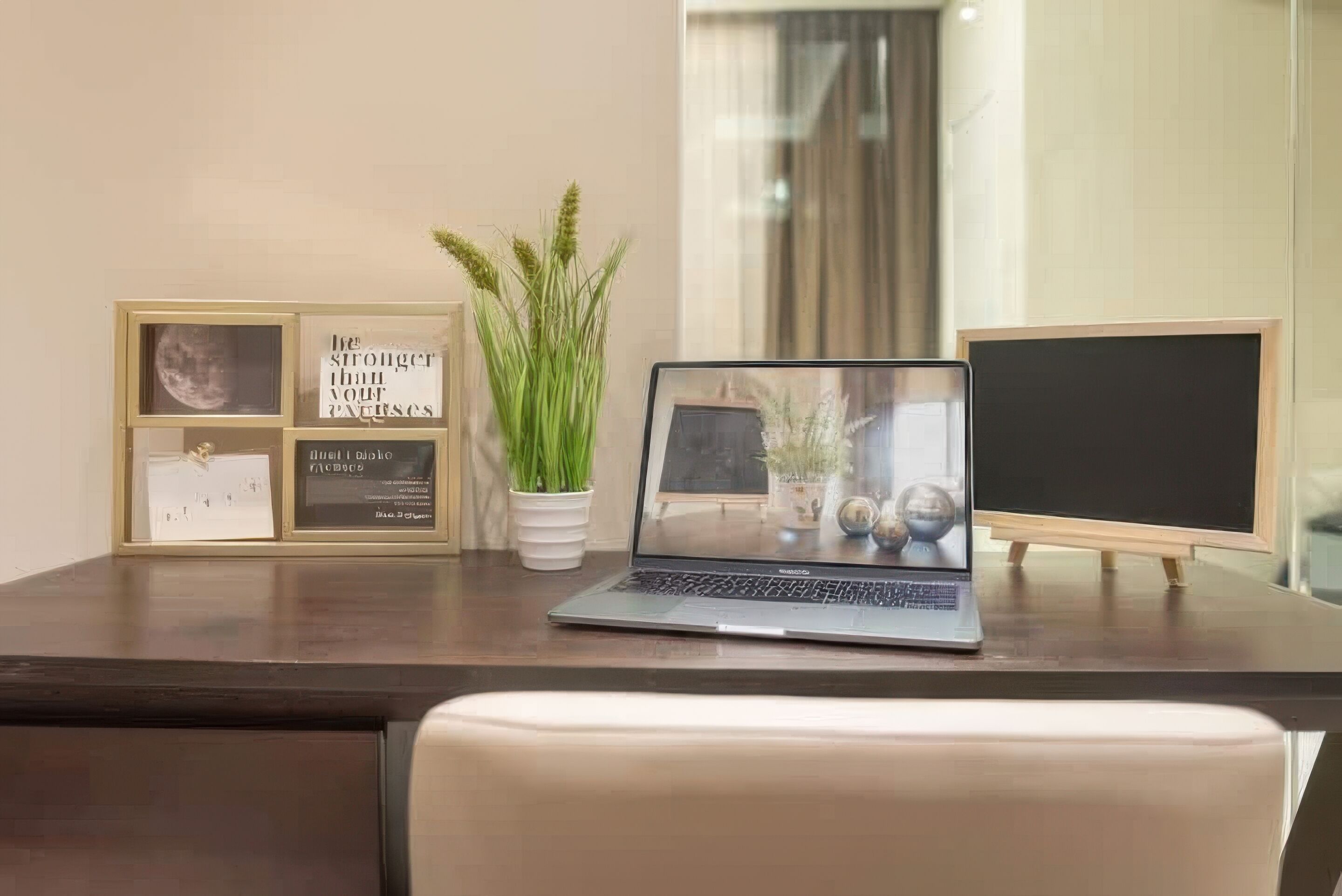 A laptop on a desk with framed motivational quotes, a potted plant, and a chalkboard.