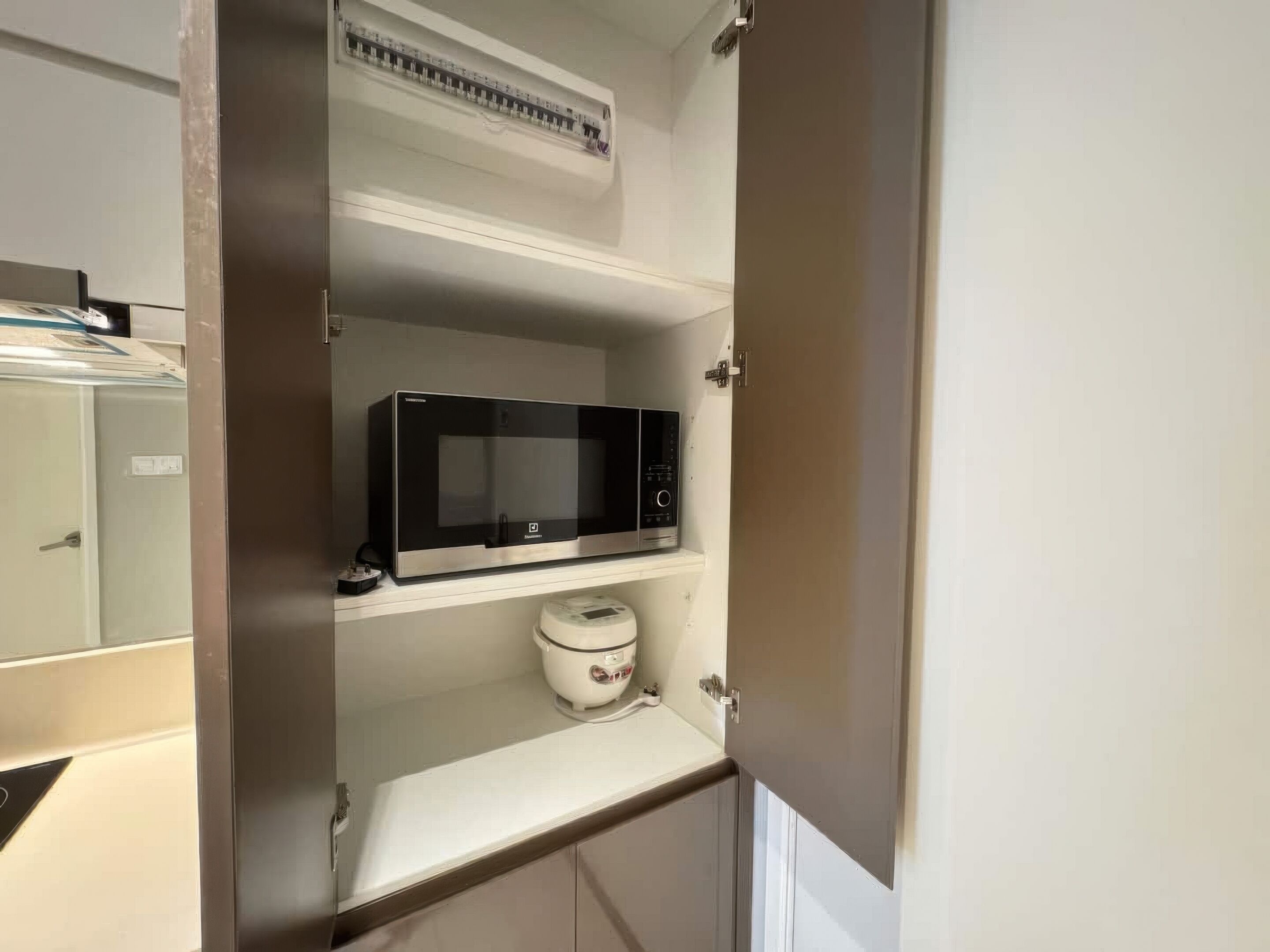 A kitchen with a microwave on the upper shelf and a rice cooker on the lower shelf.