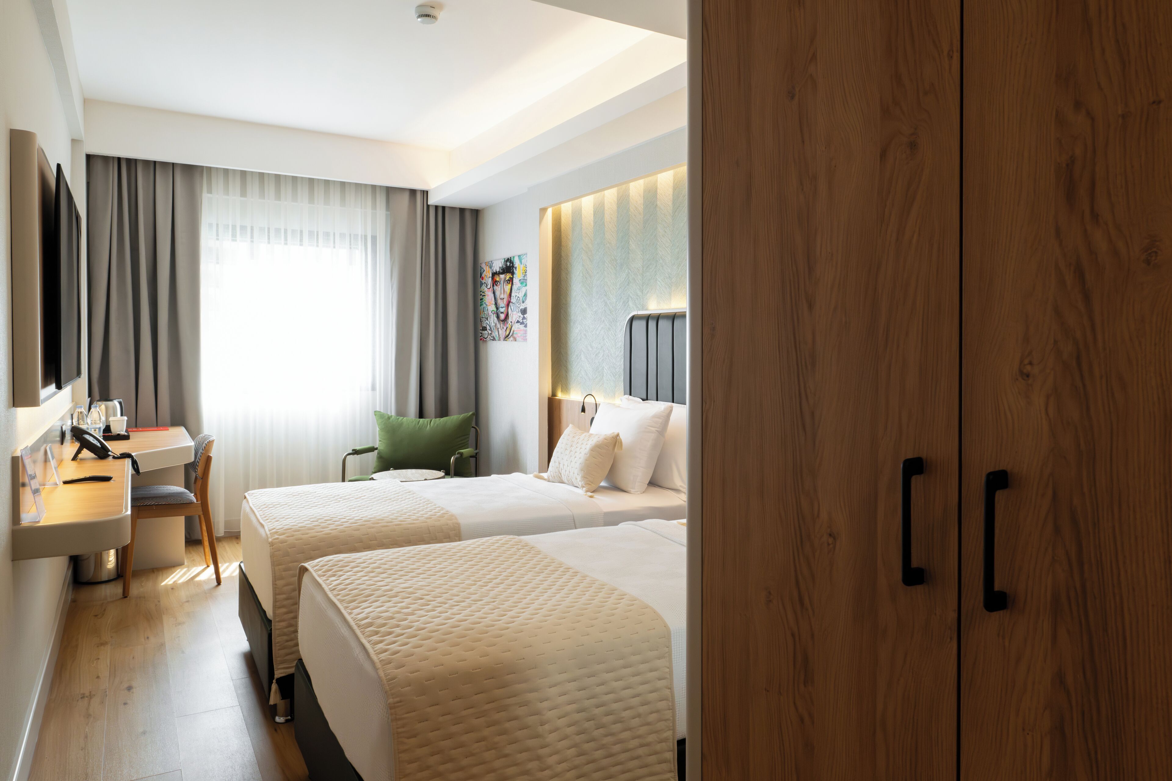 Ein Hotelzimmer mit zwei Betten, einem Schreibtisch mit Stuhl, einem Fernseher und einem großen Holzschrank.