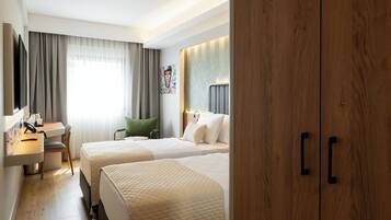 Ein Hotelzimmer mit zwei Betten, einem Schreibtisch mit Stuhl, einem Fernseher und einem großen Holzschrank.