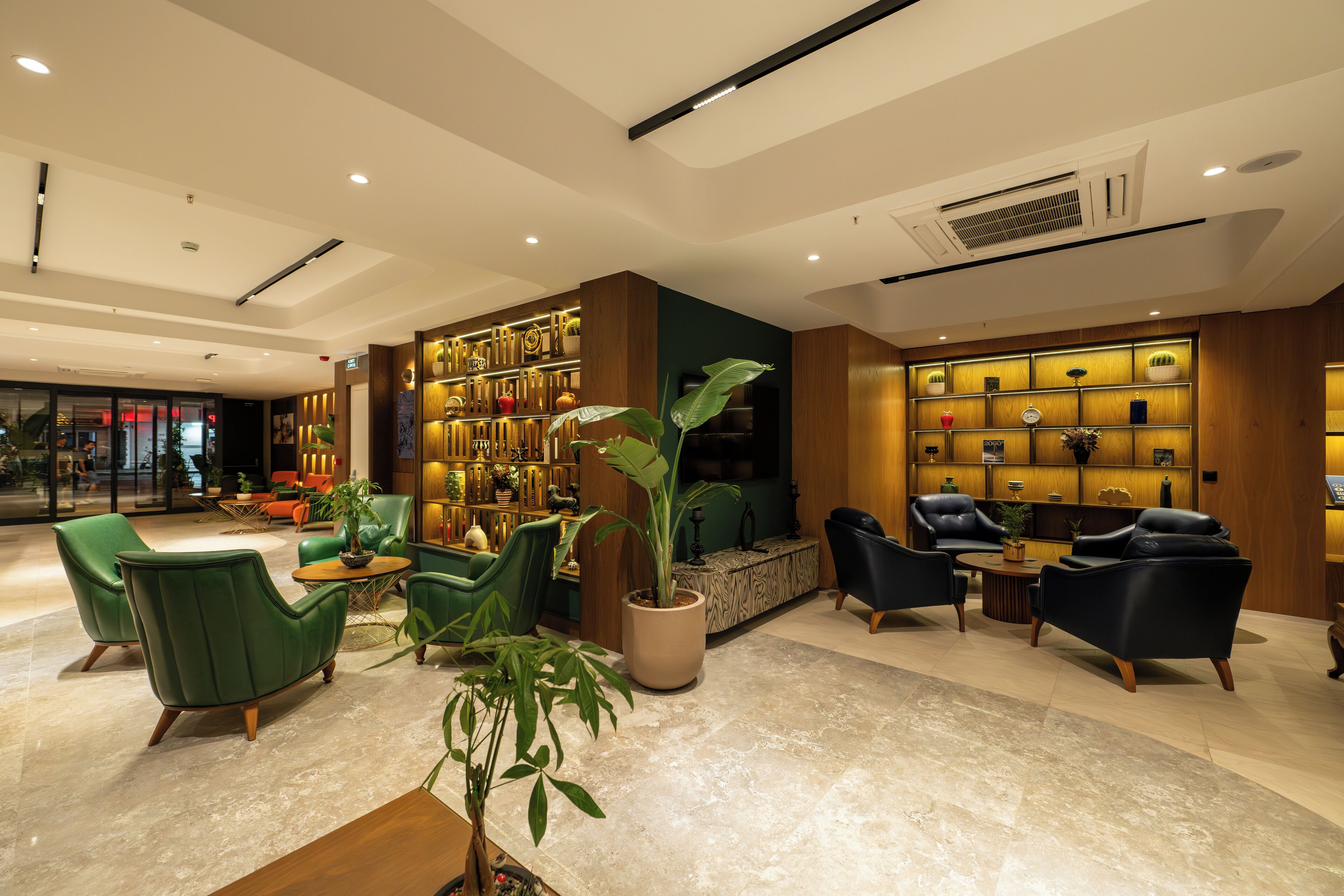 A modern lobby with green and black leather chairs, a large potted plant, and a wall of decorative items.