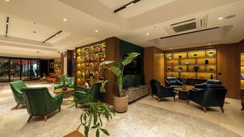 A modern lobby with green and black leather chairs, a large potted plant, and a wall of decorative items.