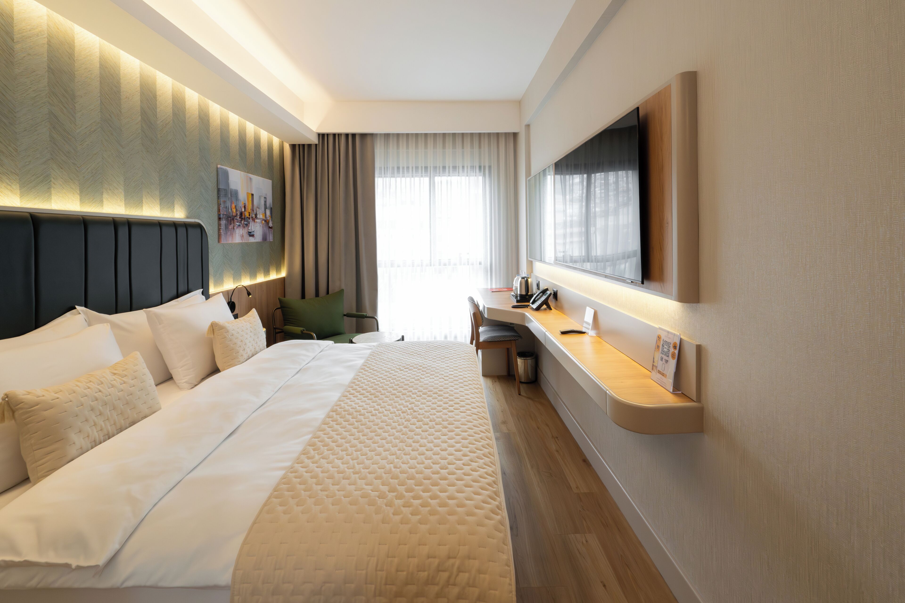 Habitación de hotel con una cama grande, un escritorio, una silla, un televisor de pantalla plana montado en la pared y una ventana con cortinas.