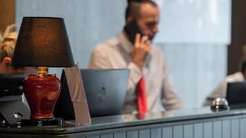 A reception desk with a red vase lamp, laptops, and a blurred background of a person on the phone.
